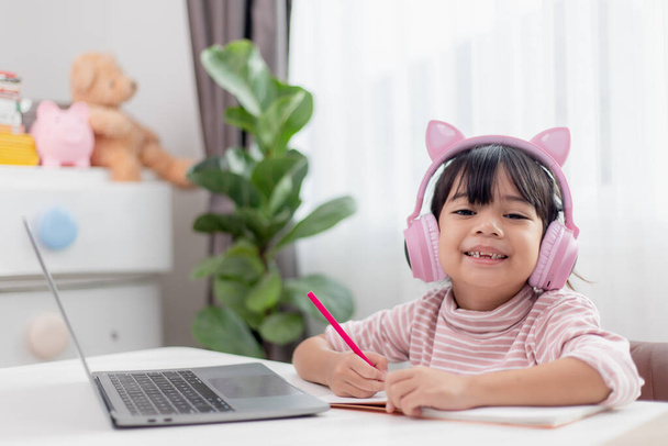 Kulaklık takan Asyalı küçük kız, bilgisayar kullanan öğretmeniyle uzaktan video görüşmesi yapıyor, internette çalışıyor, evde eğitim kavramı geliştiriyor. - Fotoğraf, Görsel