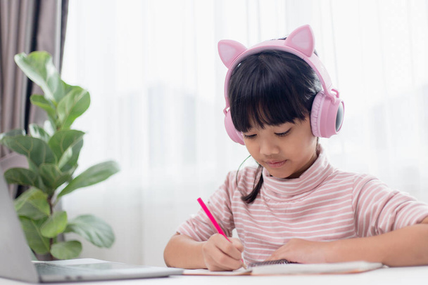 Aasialainen pieni tyttö kuulokkeissa on videopuhelu kaukainen luokka opettajan kanssa kannettavan tietokoneen avulla, opiskele verkossa tietokoneella, kotiopetuksen käsite - Valokuva, kuva