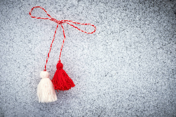 martenitsa. Bulgarian Symbols of spring. Red and white tassels of threads on the ground covered with snow. Baba Marta Day. Wallpaper of spring flowers. - Photo, image