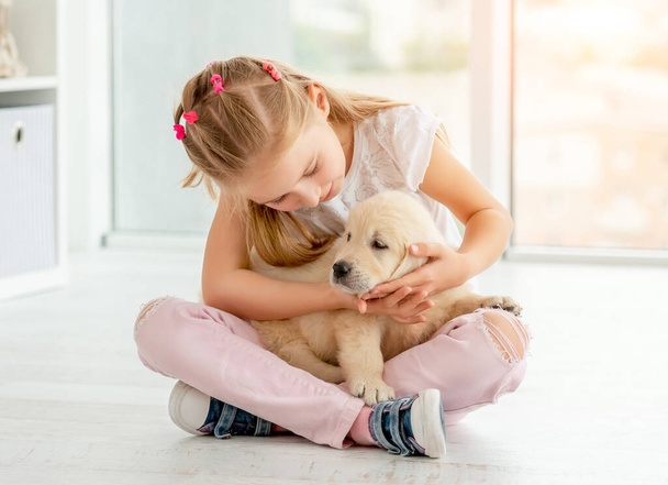 Lovely girl looking at puppy sitting on the floor - Фото, изображение