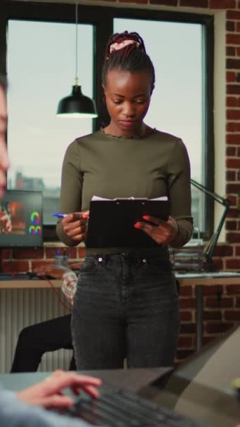 Függőleges videó: afro-amerikai női alkalmazott olvasás dokumentáció munka digitális ügynökség iroda, mosolygós művészeti tervező. Nő nézi vágólap fájlok használata előtt 3D szoftver interfész. - Felvétel, videó