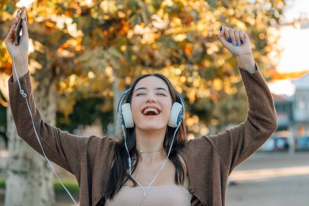 girl in autumn excited with happiness with headphones and mobile phone - Photo, Image