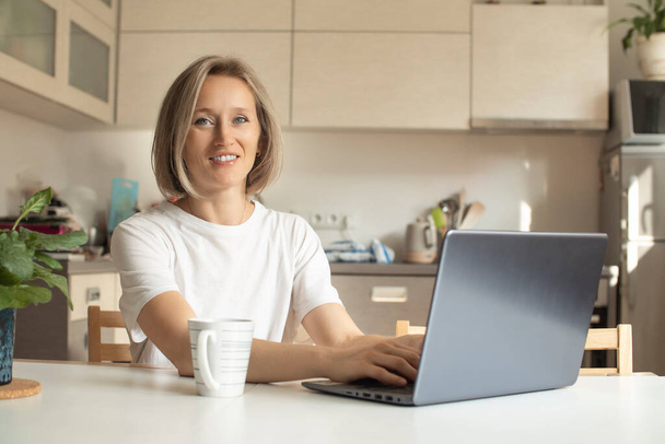 mujer joven en la cocina con una taza y un ordenador portátil - Foto, imagen