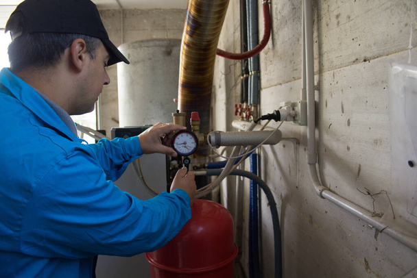 Vízvezeték szerelő munkaruhában javítás és karbantartás egy házi kazán. A kazán bekapcsolása a télre való felkészülésben - Fotó, kép