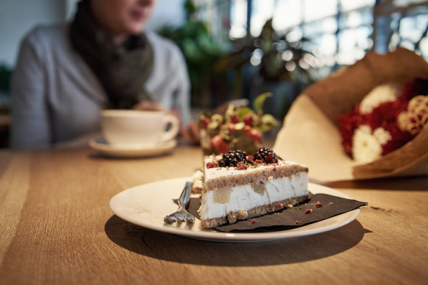 Ik stuk zoete taart in een cafe, met een vrouw die werkt op de mobiele telefoon op de achtergrond - Foto, afbeelding