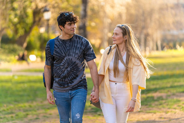 Nuoren heteroseksuaalisen pariskunnan muotokuva kävelemässä puistossa, jolla on defocked tausta ja etsivät toisiaan - Valokuva, kuva
