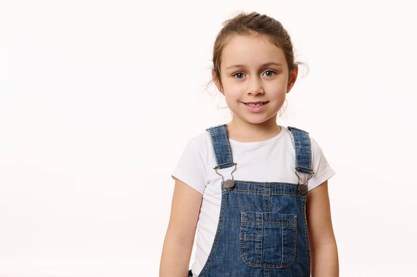 Emotional portrait isolated on white background of a delightful Caucasian baby girl, wearing blue denim overalls, happily smiling looking at camera. Beautiful kids. Children. Happy childhood concept - Photo, image