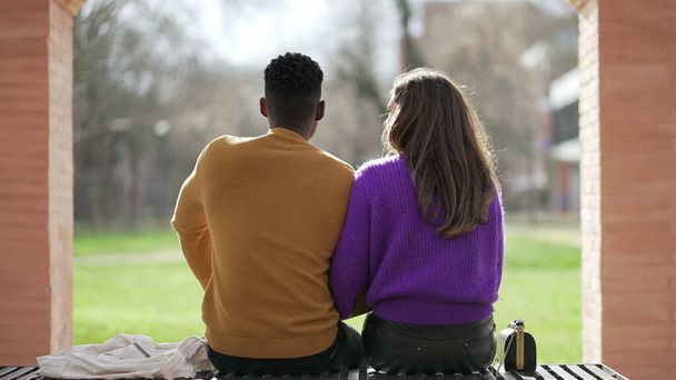 Back of interracial couple sitting on bench outside - Fotoğraf, Görsel