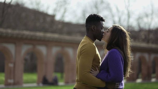 Black man kissing white girlfriend standing outside at park - Φωτογραφία, εικόνα
