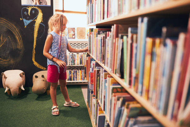 Schoolgirl looking for book for reading in school library. Student choosing literature for reading. Books on shelves in bookstore. Learning from books. Back to school. Elementary education. Doing homework - Φωτογραφία, εικόνα