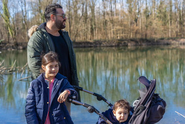 Close-up of father with stroller and two children walking along the Aare river in riparian forest in springtime. - Photo, Image