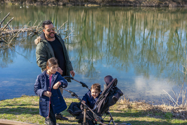 Isä rattaiden kanssa ja kaksi lasta kävelemässä Aare-jokea pitkin jokimetsässä keväällä. - Valokuva, kuva