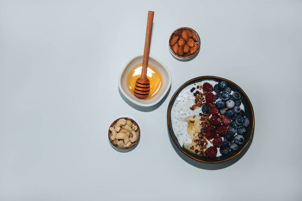 Yoghurts in green plate with blueberries, raspberries, chia seeds and granola on a white background. The concept of healthy eating. Top view - Fotó, kép