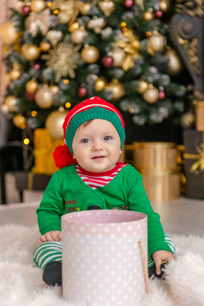 Słodki chłopiec przebrany za elfa otwiera prezent świąteczny w ozdobionym domu Bożego Narodzenia. - Zdjęcie, obraz