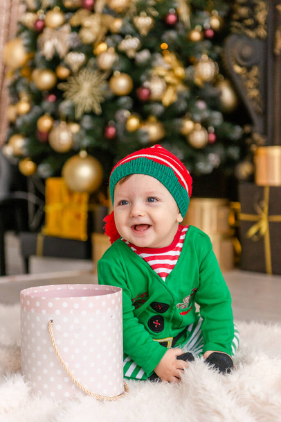 A cute little boy dressed as an elf opens a Christmas present in a decorated Christmas house. - Фото, изображение