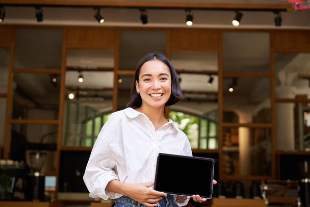 Sorridente asiatica manager femminile, proprietario del caffè, mostrando schermo tablet, dimostrando smth sul suo dispositivo. - Foto, immagini