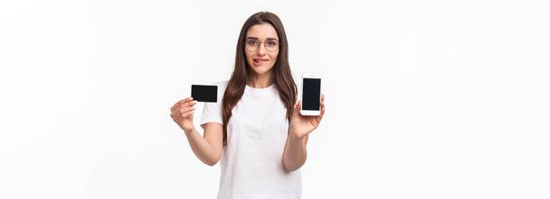 Πορτρέτο ενθουσιασμένοι και δελεαστικό νεαρή γυναίκα αρέσει ψώνια, ανυπομονούν να χρησιμοποιήσουν τη νέα πιστωτική της κάρτα στο ηλεκτρονικό κατάστημα, δείχνει οθόνη του κινητού τηλεφώνου, καυχηθεί με τραπεζικό λογαριασμό της, δάγκωμα χείλος ενθουσιασμένος. - Φωτογραφία, εικόνα