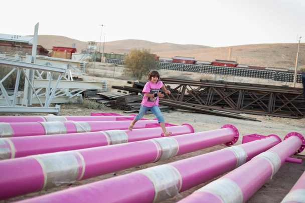 A cute caucasian boy is playing and running barefoot in a pink stylish t-shirt with a cat print among pink iron pipes on an industrial background. Fashion photography - Photo, Image