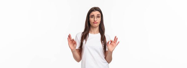 Not bad, very cool. Waist-up portrait of impressed young pretty woman in glasses, smirk and show okay signs, pleased with great choice, rate awesome product, standing white background. - Photo, Image