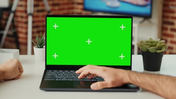 デスクで緑色のスクリーンテンプレートを使用してノートパソコンで作業している若い成人は、空白のクロマキーとポータブルコンピュータ上の隔離されたディスプレイを確認します。コピースペースをモックアップしたPCを見てください。三脚が撃たれた。閉じろ!. - 映像、動画