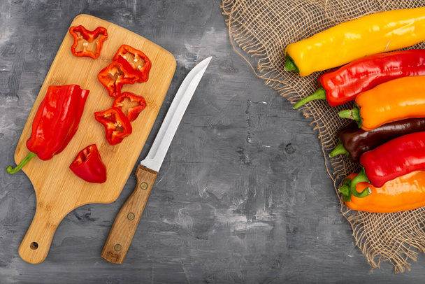 Fresh sweet pepper (bell pepper) on a cutting board with a knife. Chopped pepper pieces are ready to cook. On a gray background, top view. - Fotografie, Obrázek