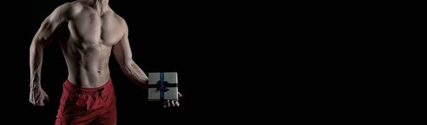 muscular man with gift box. present from man with muscular torso isolated on black. banner of muscular man with gift, copy space. man with muscular torso hold gift. - Photo, Image