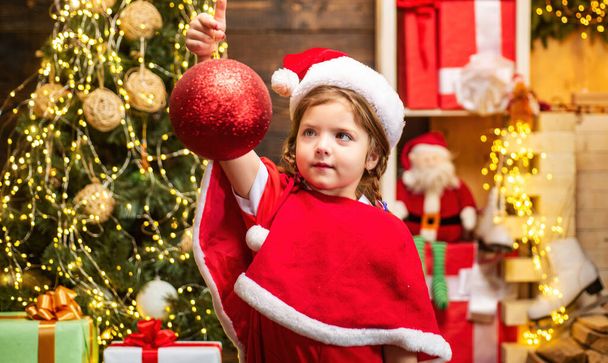 Child decorating with bauble or Christmas ball Christmas tree - Foto, Imagen