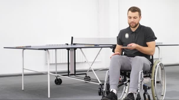 Nuori vammainen kaveri pyörätuolissa pelaa pöytätennistä. Urheilijalla on vaurioitunut moottori - Materiaali, video