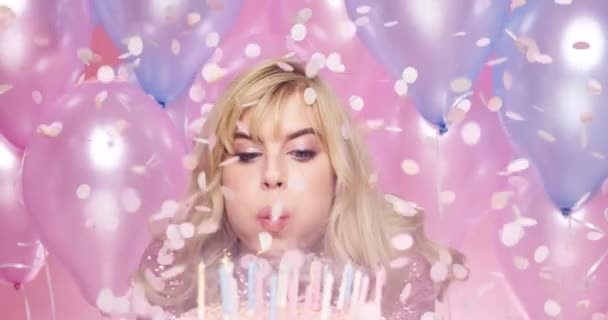 Confetti, happy and party woman tort urodzinowy na świętowanie z podekscytowaną twarzą na specjalne wydarzenie. Uśmiech, świętować i szczęśliwy solenizantka dmuchanie świece ciasto z kolorowe balony pastelowe - Materiał filmowy, wideo