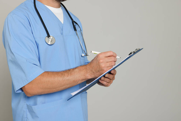 Doctor with stethoscope and clipboard on light grey background, closeup - Fotografie, Obrázek