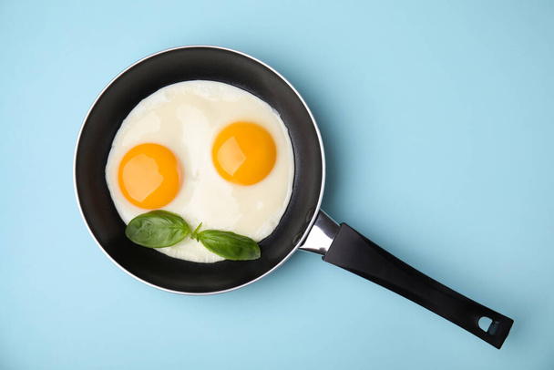 Tasty fried eggs with basil in pan on light blue background, top view - Photo, image