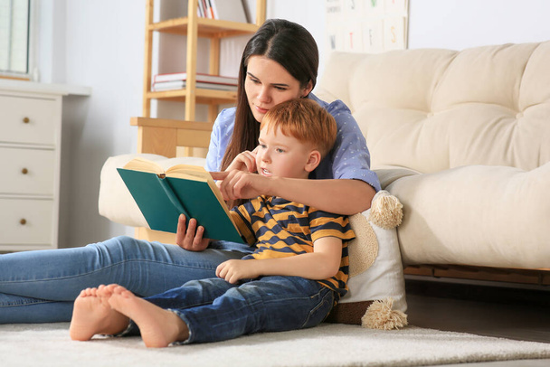 Mother reading book with her son in living room at home - Foto, imagen