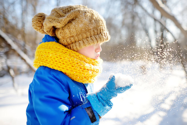 Little boy blowing snow from his hands. Child enjoy walking in the park on snowy day. Baby having fun during snowfall. Outdoor winter activities for family with kids. - Zdjęcie, obraz