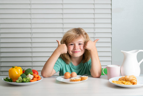 Funny blonde little boy having breakfast. Milk, vegetables and fruits healthy food nutrition for children - 写真・画像