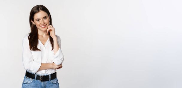 Smiling young businesswoman, female entrepreneur in white shirt, cross arms on chest like professional, standing over studio background. - Foto, immagini