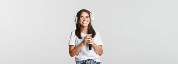 Atraktivní usměvavá brunetka ve sluchátkách, zpívající karaoke, držící mikrofon. - Fotografie, Obrázek