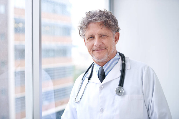Il s'occupe de votre santé. Portrait d'un médecin mature souriant debout dans son bureau - Photo, image