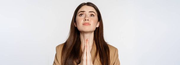 Hopeful corporate woman, student praying, begging god, looking up and pleading, standing over white background. Copy space - Foto, afbeelding
