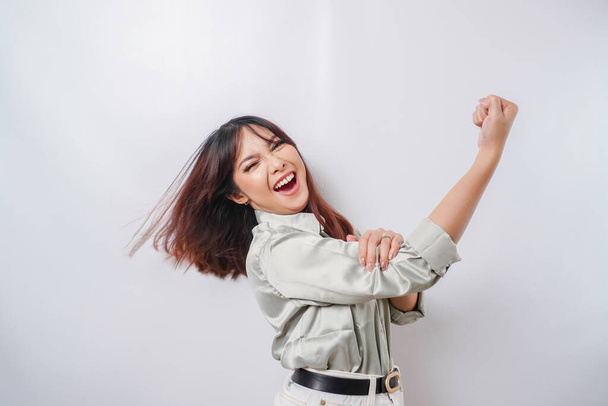 Excited Asian woman wearing a sage green shirt showing strong gesture by lifting her arms and muscles smiling proudly - Photo, Image