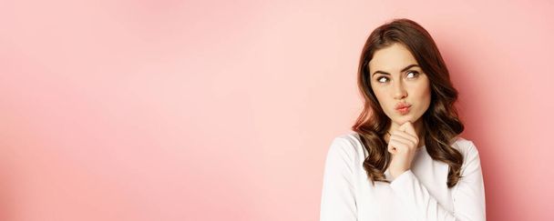Close up portrait of coquettish smiling woman, glamour girl thinking, looking thoughtful, standing over pink background. - Foto, Imagen