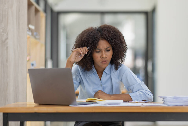 アフリカ系アメリカ人の家族はノートパソコンで仕事をしながらストレスを感じ、職場のコピースペースで頭痛の種を感じる疲れた悲しい女性.  - 写真・画像