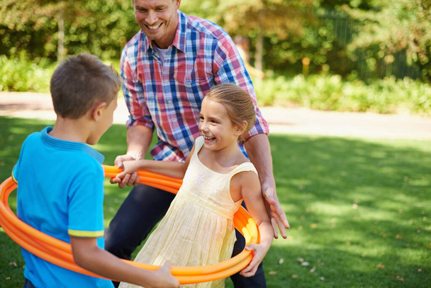 Spaß im Park. Eine glückliche junge Familie spielt an einem sonnigen Tag im Park mit Hula-Hoop-Reifen - Foto, Bild