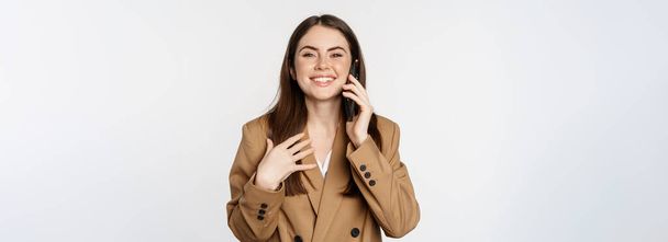 Бізнес-леді, що має мобільний дзвінок, розмову на смартфоні, розмовляє з клієнтом, стоїть над білим тлом у коричневому костюмі
. - Фото, зображення