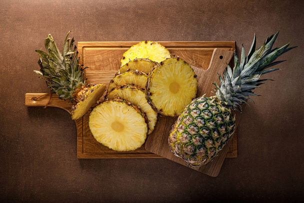 Pineapple. Sliced and whole pineapple on brown background, top view - Zdjęcie, obraz