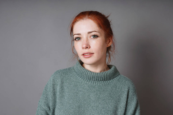 mid adult woman with red hair green eyes and turtleneck sweater against gray background with copy space - Photo, Image