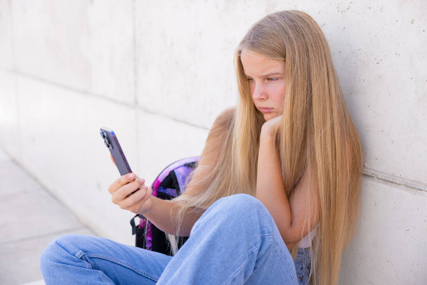 Ragazza adolescente seduta da sola fuori e guardando il telefono cellulare - Foto, immagini