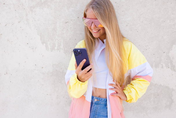 Uśmiechnięta nastolatka stojąca na zewnątrz i korzystająca z telefonu komórkowego - Zdjęcie, obraz