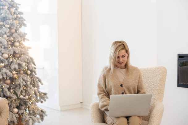 Возбужденная улыбающаяся женщина имеет ноутбук видео чат. Молодая женщина дома в счастливом рождественском настроении - Фото, изображение