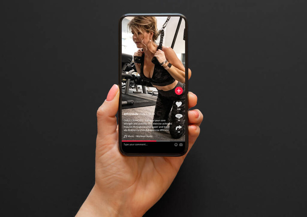 Βίντεο με μια γυναίκα που εργάζονται σε ένα γυμναστήριο μοιράζονται σε εφαρμογή κοινωνικών μέσων μαζικής ενημέρωσης που προβάλλονται σε ένα κινητό τηλέφωνο - Φωτογραφία, εικόνα