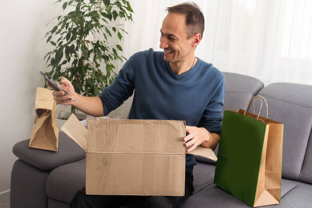 Bello scatola di apertura giovane uomo con pacco mentre seduto sul divano a casa
 - Foto, immagini
